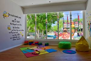 Kinderspielzimmer im Hotel Kandima Maldives mit bunten Spielmatten, Spielzeug und Blick auf einen Spielplatz.
