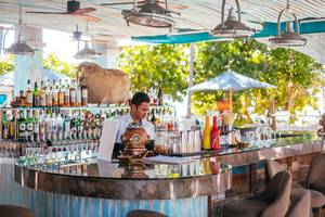 Ein Barkeeper serviert Getränke hinter einer Theke im Freien im Finolhu Baa Atoll Hotel auf den Malediven.