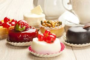 Verschiedene Desserts auf einem Holztisch, darunter eine Tarte mit Himbeeren und eine Schokoladentarte.