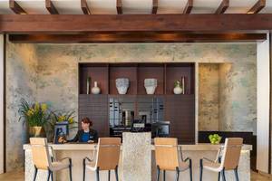 Empfangsbereich des H10 Estepona Palace Hotels mit Rezeptionistin, Vasen und Pflanzen im Hintergrund.