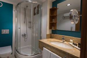 Badezimmer im Kamelya Aishen K Club Hotel mit Glasdusche, Waschbecken und Spiegel.