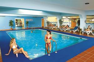 Zwei Frauen am Rand eines Innenpools im Nestor Hotel, eine sitzt und die andere steht neben ihr.