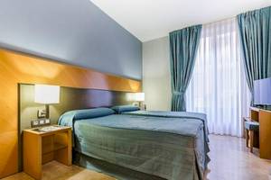 Doppelbettzimmer im Del Mar - Barcelona Hotel mit blauen Vorhängen und Holzmöbeln.