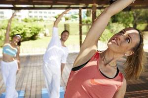 Gruppe von Menschen, die Yoga auf einer Terrasse im Freien im Robinson Kyllini Beach Hotel praktizieren.