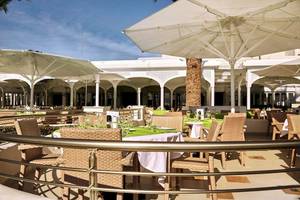 Außenterrasse des Robinson Kyllini Beach Hotels mit Tischen und Stühlen unter Schirmen.