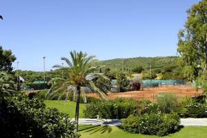 Tennisplatz im Freien im Robinson Kyllini Beach Hotel mit grünem Rasen und Palmen.