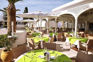Außenbereich des Robinson Kyllini Beach Hotels mit gedeckten Tischen und weißen Sonnenschirmen.