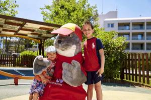 Zwei Kinder stehen neben dem Maskottchen von Robinson Kyllini Beach Hotel im Spielplatz.