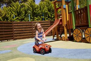 Ein kleines Mädchen spielt auf einem roten Spielzeugauto im Spielplatz des Robinson Kyllini Beach.