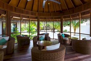 Loungebereich im Amaya Kuda Rah Hotel mit Korbsesseln, Tischen und Glaswänden.