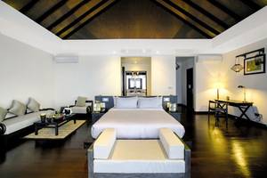 Ein modernes Hotelschlafzimmer im Atmosphere Kanifushi Maldives mit weißen Möbeln und Holzboden.