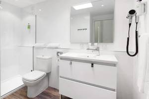 Ein modernes Badezimmer mit weißer Dusche, Toilette, Waschbecken und Spiegel im Sol Fuerteventura Jandia Hotel.