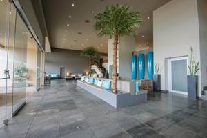 Lobby des Oasis Salinas Sea Hotels mit gepolsterten Bänken, Palmen und blauen Vasen.