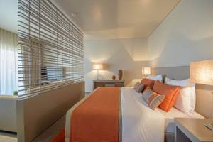 Schlafzimmer im Oasis Salinas Sea Hotel mit einem großen Bett, weißen und orangefarbenen Kissen und Nachttischen mit Lampen.