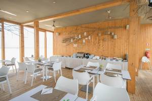 Innenansicht des Restaurants im Oasis Salinas Sea Hotel mit weißen Tischen und Stühlen und hölzernen Wänden.