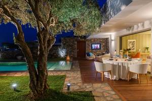 Außenbereich des Elounda Beach Hotel & Villas bei Nacht mit Swimmingpool und Esstisch.