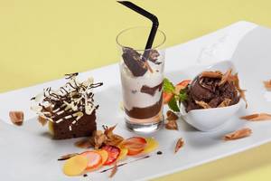 Ein weißer Teller mit einem Brownie, einem Glas mit Schokoladengetränk und Eiscreme sowie einem Eiskübel.