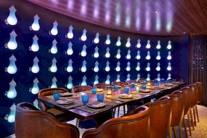 Restaurant im W Muscat Hotel mit langer Tafel und blauer Wandbeleuchtung.