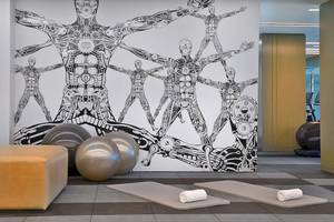 Fitnessraum im W Muscat Hotel mit einer Wandgestaltung von menschlichen Figuren und Fitnessgeräten.