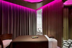 Behandlungsraum im W Muscat Spa mit violetten Lichtern und einem Massagebett.