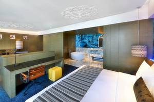 Innenansicht der Suite im W Muscat Hotel mit Bett, Schreibtisch, Sessel und Badezimmer mit Badewanne