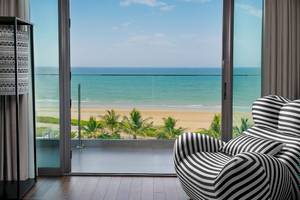 Blick aus einem Hotelzimmer auf das Meer mit einer schwarzen und weißen gestreiften Liege und einem Glasfenster.