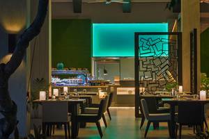 Innenbereich des Restaurants im Velassaru Maldives Hotel mit blau beleuchteter Wand und gedeckten Tischen.