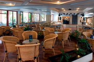 Innenbereich des Puerto Palace Hotels mit runden Tischen und Stühlen aus Rattan.