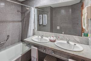 Badezimmer im Puerto Palace Hotel mit Badewanne, zwei Waschbecken, Handtuchhaltern und Spiegel.