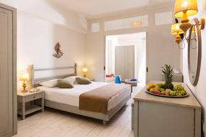 Innenansicht eines Schlafzimmers im Almyrida Beach Hotel mit Bett, Nachttischen und Obstplatte.