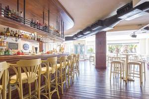 Bar im Be Live Experience Lanzarote Beach Hotel mit gelben Stühlen und einer Theke mit Flaschen.