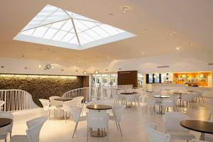 Innenbereich des Be Live Experience Lanzarote Beach Hotels mit vielen Tischen und Stühlen, hoher Glaskuppel und Steinwand.