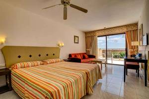 Schlafzimmer im SBH Taro Beach Hotel mit zwei Betten, Wohnzimmersofa, Schreibtisch und Terrassenzugang.