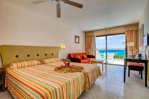 Hotelzimmer mit Meerblick, Bett, Couch, Tisch und Balkon.