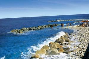 Strand mit Felsen und Meer im Hintergrund, einige Menschen baden und entspannen