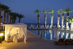 Nachtansicht des Vrissiana Beach Hotel mit Pool und Liegestühlen unter Palmen.