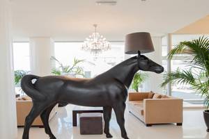 Ein großes schwarzes Pferde-Design, das als Lampenschirm dient, steht in einer eleganten Hotellobby.