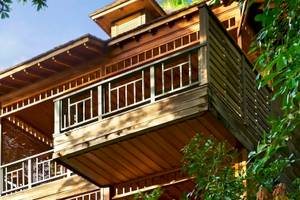 Ein zweistöckiges Holzhaus mit Balkon, umgeben von Bäumen, im Hilton Seychelles Northolme Resort & Spa.