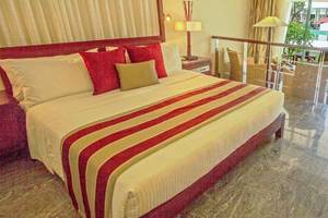 Hotelzimmer im Occidental Eden Beruwala mit großem Bett, roten Kissen, und Glasbalkon.