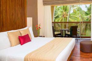 Hotelzimmer des Occidental Eden Beruwala mit einem Bett, Balkon und Aussicht auf Palmen.