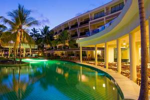 Ein großer Swimmingpool mit leuchtend grünem Wasser, umgeben von Palmen, vor dem Occidental Eden Beruwala Hotel bei Nacht.