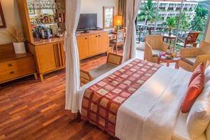 Ein elegantes Hotelzimmer im Occidental Eden Beruwala mit einem großen Bett, Holzmöbeln und einer Aussicht auf den Garten.