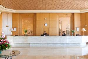 Rezeptionsbereich des El Mouradi Hammamet Hotels mit zwei Mitarbeitern und Blumenarrangements.