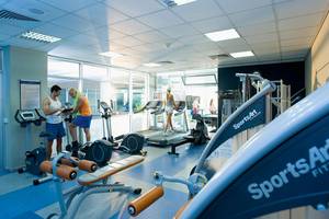 Fitnessstudio im Mediterranean Beach Hotel Zypern mit mehreren Trainingsgeräten und Personen.