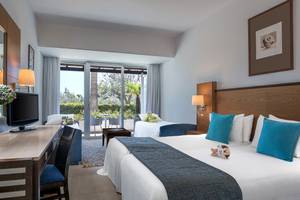 Doppelzimmer im Mediterranean Beach Hotel in Zypern mit zwei Betten, Fernseher, Schreibtisch und Balkonzugang.