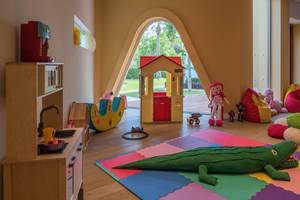 Ein Kinderzimmer mit einer Spielmatte, Spielzeug, einem Haus, Puppen und einer Küche.