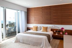 Schlafzimmer mit Balkon im Mediterranean Beach Hotel in Zypern, mit modernen Holzwänden, einem großen Bett und einem Ausblick auf das Meer.