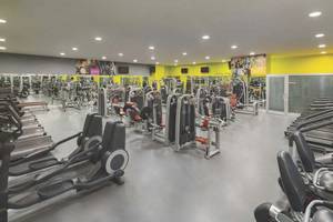 Fitnesscenter des Wyndham Grand Izmir Ozdilek Hotels mit vielen Geräten und gelben Wänden.