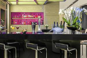 Innenansicht der Bar im H10 London Waterloo Hotel mit schwarzem Tresen, Cocktails, Trophäe, Pflanzen und Dekor.