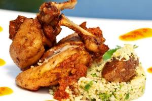 Gebratenes Huhn mit Couscous und Soßen auf einem weißen Teller serviert.